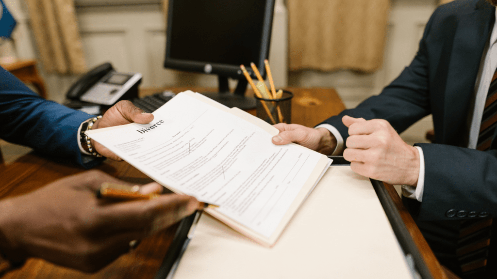 Two individuals in suits sitting at a desk signing papers