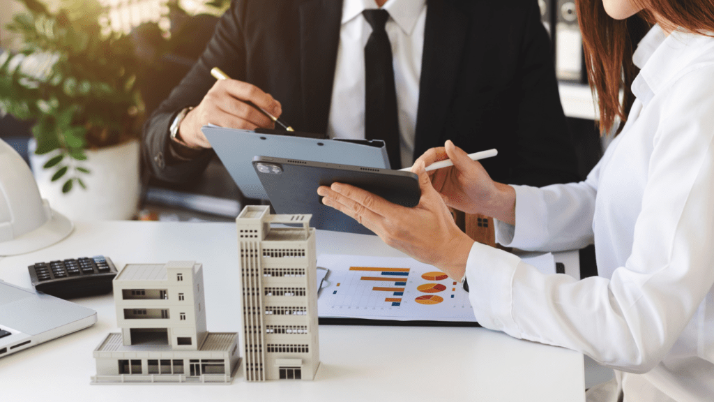 Two people in business attire sitting at a table with paper and a tablet