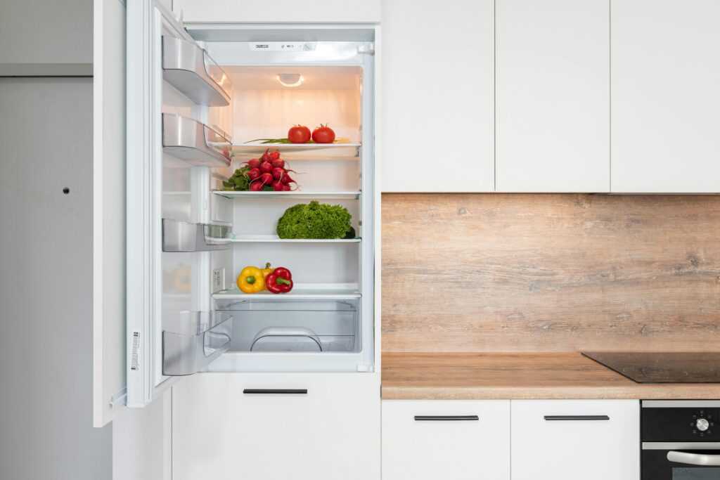 Open fridge in a sleek kitchen with fresh vegetables, perfect for healthy meals.
